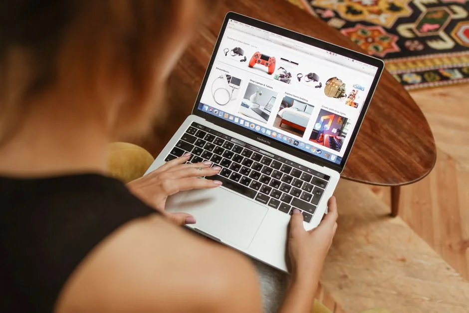 about-04 An anonymous woman in jeans and a light blue shirt is shown from above, working at a desk with gadgets and papers while flipping through a magazine and drinking a cup of hot americano